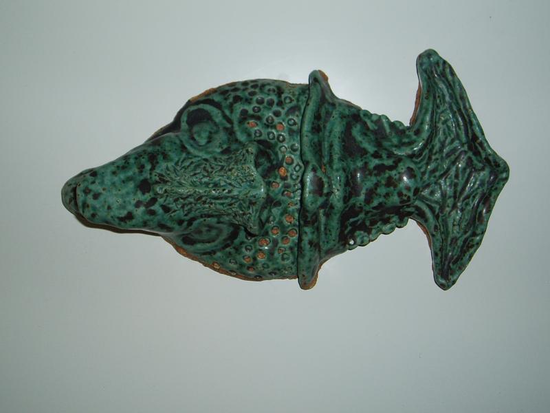 A mask in the shape of a fish when turned sideways, and a human face when turned right side up. Glazed with green glaze.