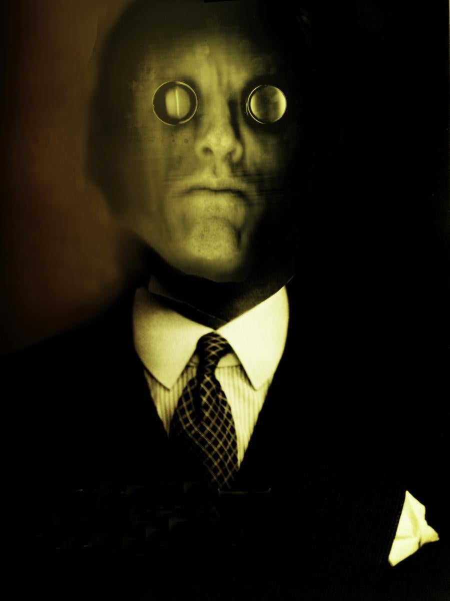 A scanograph, photomontage color self- portrait depicting me with a lizard’s face with magnifying lenses over my eyes. I am wearing a business suit and tie. This image is from my “Transmog Project” body of work.