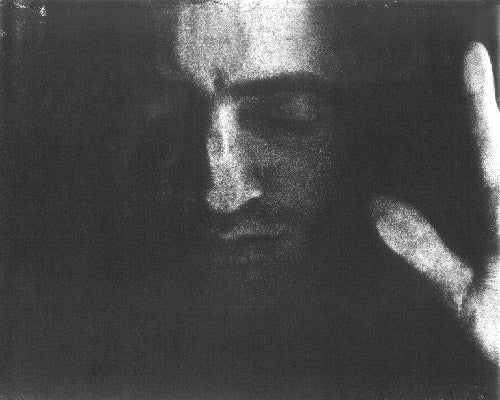 A Black & White scanographic self-portrait from my “Blind Vision” series. This is a frontal portrait. My eyes are closed and surrounded in darkness. I have a calm almost serene expression on my face. My thumb and forefinger from my right hand appear on the very edge of the frame.  