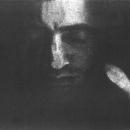 A Black & White scanographic self-portrait from my “Blind Vision” series. This is a frontal portrait. My eyes are closed and surrounded in darkness. I have a calm almost serene expression on my face. My thumb and forefinger from my right hand appear on the very edge of the frame.  