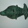 A mask in the shape of a fish when turned sideways, and a human face when turned right side up. Glazed with green glaze.