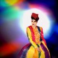 A photomontage of a runway model wearing a rainbow-colored dress. Her torso is twisting as she pivots the runway. A spotlight beam positioned directly behind her head enshrouds her in a halo. The light splinters and fragments into various rainbow colors. This image is from my “Neo Glam” series of reimagined fashion portraits.