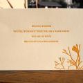 Photo of a postcard with orange text and a flower on the bottom right.